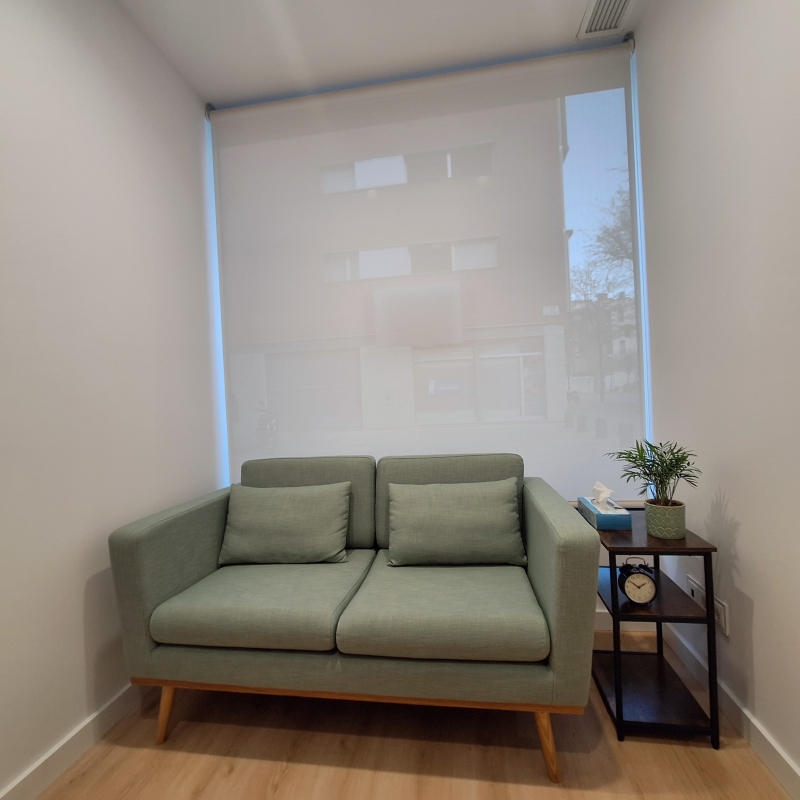A sofa for two. Next to it stands a small rack with handkerchiefs, an alarm clock and a small plant on it.