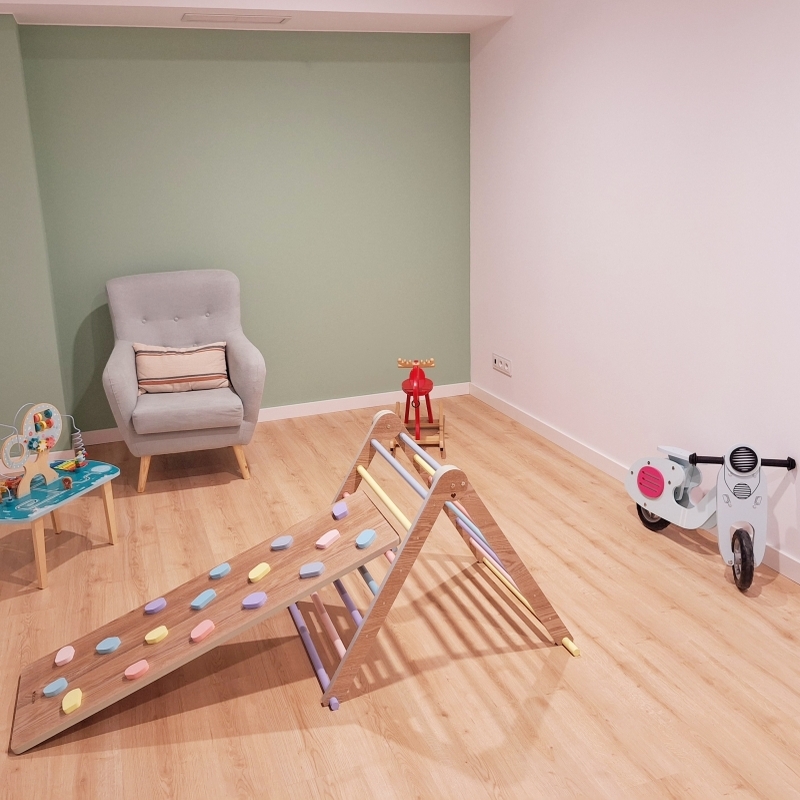 A table with two chairs facing each other. On a shelf there are some books. On the wall there are three pictures.